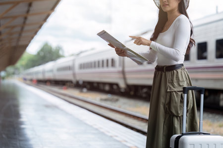 Young woman female traveler looking on map while waiting for the train at train stationの写真素材