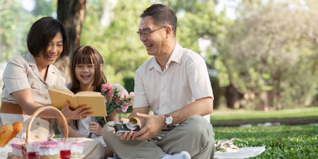 happy smiling family grandparent and grandchild picnic together outside at parkの写真素材