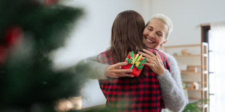 Thankful Caucasian woman with christmas gift hugging daughter at homeの写真素材