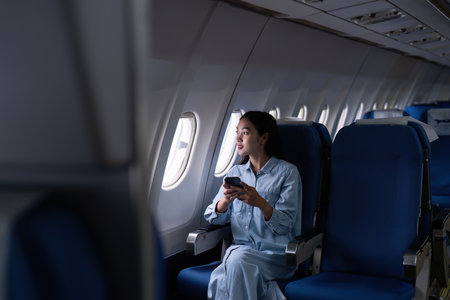 Asian people female person onboard, airplane window, using mobile while on the planeの写真素材