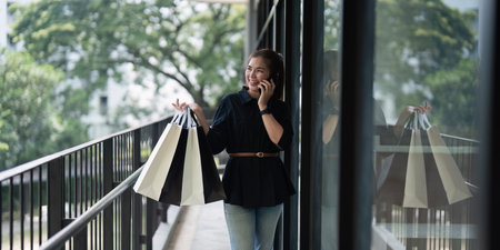 Young woman standing at road holding shopping bags and using mobile phone. Purchases, black friday, discountの写真素材