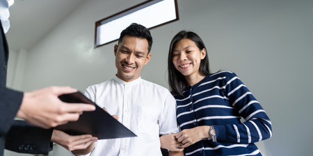 Young happy smiling couple read agreement with realtor and looking through the contract of real estate sale going to signing a dealの写真素材