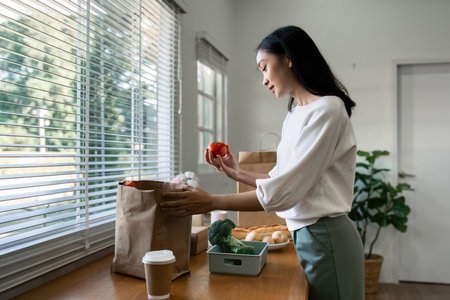 Organic Food Delivery. Happy young woman unpacking bag with Fresh Vegetables in kitchenの写真素材