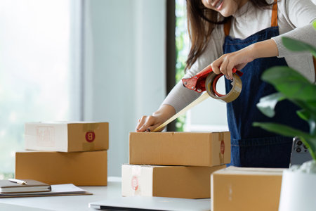 Young business entrepreneur sealing a box with tape. Preparing for shipping, Packing, online selling, e-commerce conceptの写真素材