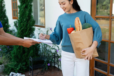 Asian woman signing the receipt on the order receipt through the online supermarkets home storeの写真素材