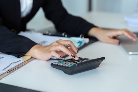 Businesswoman using a calculator to calculate numbers on a companys financial documents, she is analyzing historical financial data to plan how to grow the company. Financial conceptの写真素材