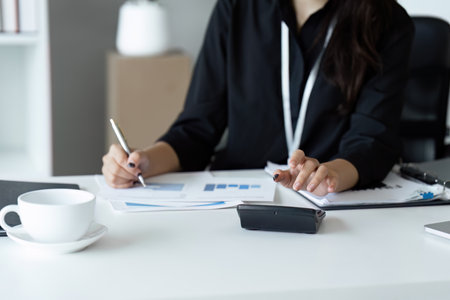 Businesswoman using a calculator to calculate numbers on a companys financial documents, she is...