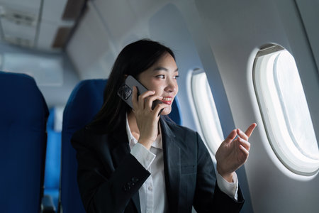 Beautiful Asian businesswoman talking with mobile phone in aeroplane. working, travel, business conceptの写真素材