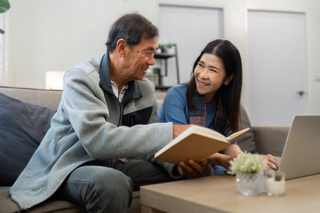Retired elderly couple sits on couch in their home reading relaxing book. Senior Activity Conceptの写真素材