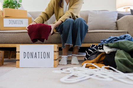 Young Asian women sit in living room sorting clothes for donation in a donation box second hand clothes. Donate conceptの写真素材