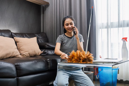 Young woman chit chat with friend on mobile while cleaning house on weekendの写真素材