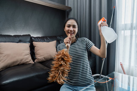 Asian woman happily use feather pick as microphone while cleaning house on the weekendの写真素材