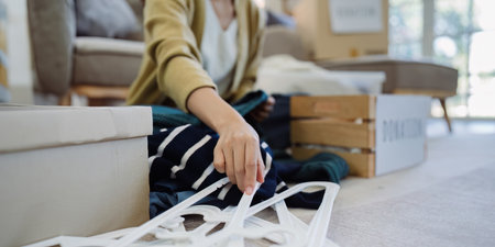 Asian young woman packing clothes at home, putting on stuff into donate box with second hand clothes. Help poor people. Donation conceptの写真素材