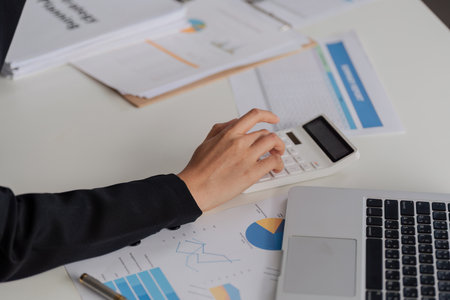 A woman is using calculator to calculate companys profit on desk with report