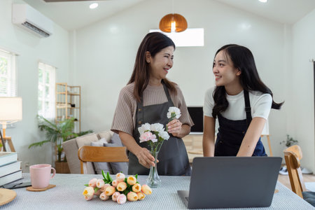 mother and daughter arrange flowers together as a hobby. mother and daughter spend free time doing flower arranging activities together and looking at laptopの写真素材