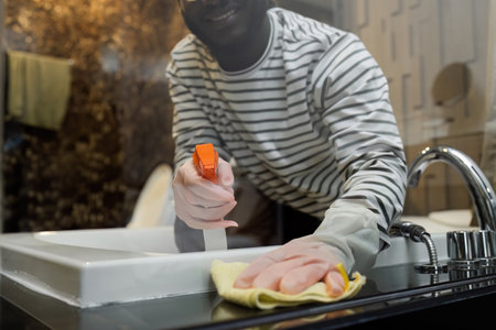 Cleaning online service. yong African American man housekeeper cleaning bathtub in bathroom with a...