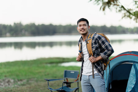 Young Adventurer Enjoying Travel Camping by the Lake with Backpack and Tent in Scenic Outdoors Settingの写真素材