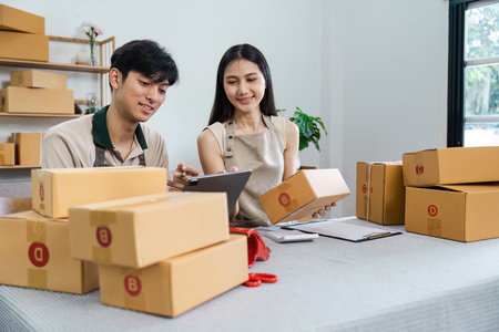 Young Entrepreneurs Managing E-Business Operations with Digital Devices and Packaging Boxes in a...