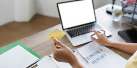 Woman Holding Credit Card for Online Shopping with Laptop and Monthly Report on Desk