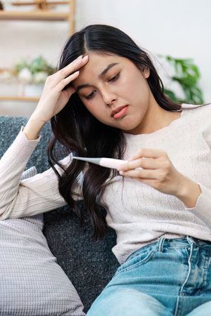 Woman Checking Thermometer for Fever While Feeling Unwell at Home on a Couch