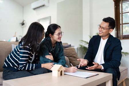 Real Estate Agent Assisting Young lgbt lesbian Couple with Signing Contract for New Home Purchase in Modern Living Roomの写真素材