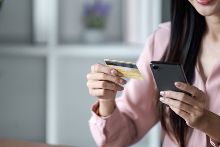 Woman Using Credit Card for Online Shopping on Smartphone in Modern Home Office Settingの写真素材