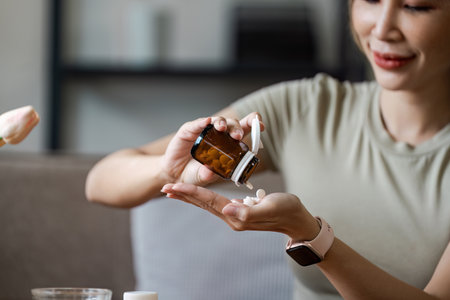 Woman Taking Pills from a Brown Bottle in a Home Setting - Healthcare and Medication Conceptの写真素材