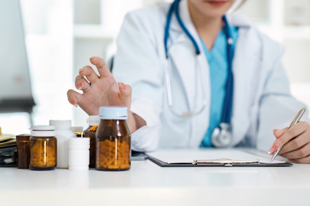 Medical Doctor Professional in White Coat with Stethoscope Reviewing Patients Prescription Bottles and Writing Notesの写真素材