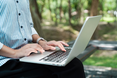 Young Digital Nomad Working Remotely on Laptop Outdoors in a Park Setting, Embracing Modern Work Flexibility and Technologyの写真素材