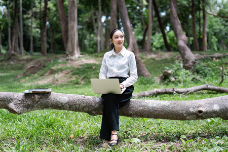 Young Digital Nomad Working Outdoors on Laptop in a Forest Setting, Embracing Remote Work and Natureの写真素材