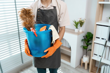 Person Holding Cleaning Supplies in a Modern Home Environment with Natural Light and Organized Shelvesの写真素材