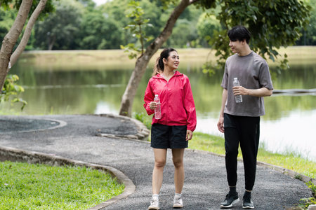 Young Couple Enjoying a Refreshing Workout Walk in a Scenic Park with Water Bottles