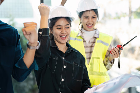 Diverse Group of Engineers Celebrating Success at Construction Site with Blueprints and Safety Gear
