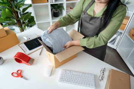 Senior Entrepreneur Packing Products for Online Business Startup in Modern Home Office with Green Plants and White Shelvesの写真素材