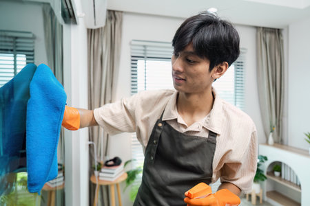 Young Man Cleaning Window with Blue Cloth and Orange Gloves in Modern Home Interior