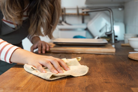 Woman Cleaning Wooden Kitchen Counter with Cloth in Modern Home Kitchen Environment