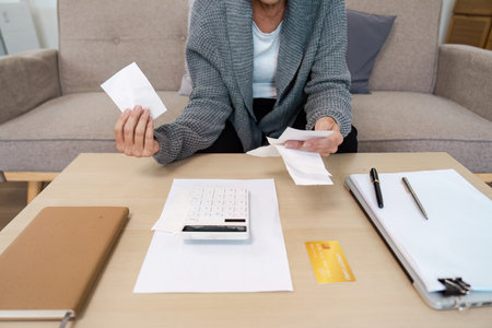 Person Calculating Bills and Expenses at Home with Calculator, Receipts, and Credit Card on Tableの写真素材