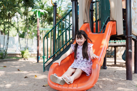 Joyful Young Girl Sliding Down Playground Slide on a Sunny Day in the Park
