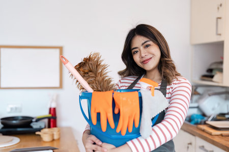 Smiling Woman Holding Cleaning Supplies and Dog in Modern Kitchen, Ready for House Cleaning Service