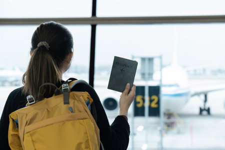 Traveler Holding Passport at Airport Terminal with Airplane in Background Ready for International...