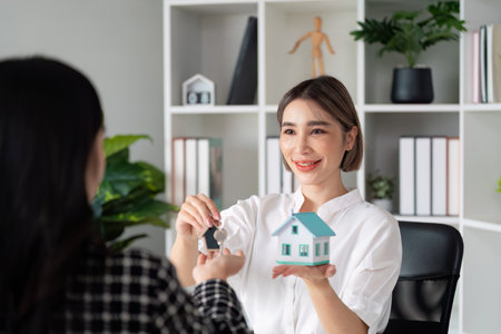 Real Estate Agent Handing Over House Keys to New Homeowner in Modern Office Settingの写真素材