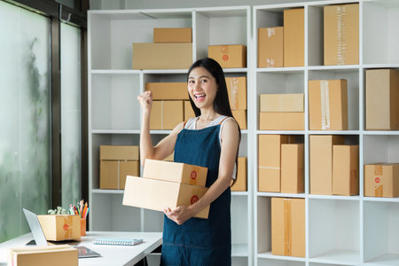 Young Entrepreneur Celebrating Success in Online Business with Shipping Boxes in Modern Home Office