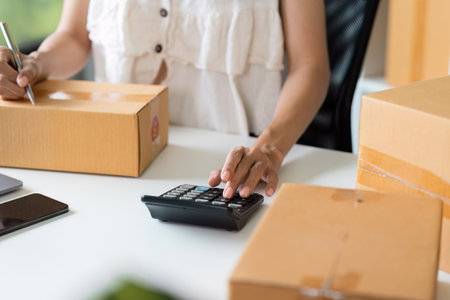 Small Business Owner Calculating finance and Managing Online Order with Cardboard Boxes on Deskの写真素材