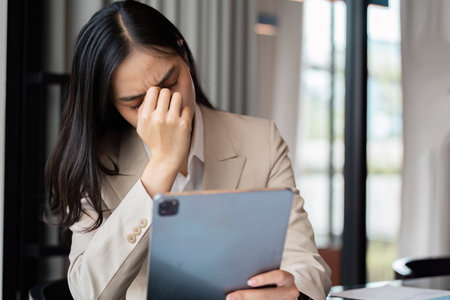 Stress Businesswoman Holding Tablet in Modern Office Environment with Natural Lightの写真素材