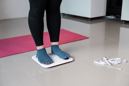 Woman Standing on Digital Scale with Measuring Tape and Yoga Mat in Modern Home Setting for Fitness and Health Lifestyleの写真素材
