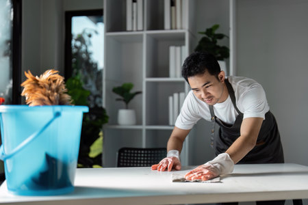 Young Man Cleaning a Modern Home Interior with a Smile, Using Eco-Friendly Products and Tools for a...