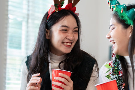 Festive Young Women Laughing and Enjoying a Holiday Party with Red Cups and Holiday Accessoriesの写真素材