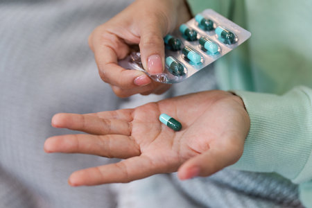 Close-Up of Hands Holding Green and Blue Capsules in Blister Pack for Healthcare and Medicine Conceptの写真素材