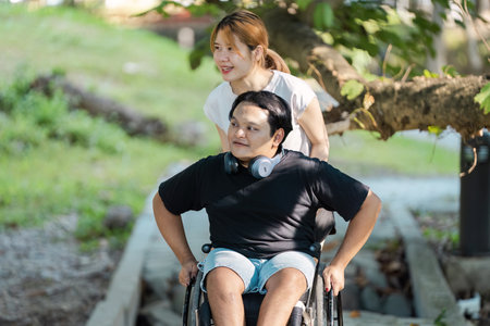 Young Woman Assisting Man in Wheelchair Outdoors on a Sunny Day in a Park Setting