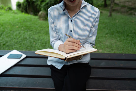 Young Professional Reading and Working Outdoors in a Park Setting with Notebook and Laptopの写真素材